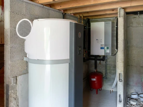 Toiture résidentielle équipée de quatre chauffe-eau solaires thermiques installés sur tuiles rouges, ciel bleu dégagé en arrière-plan avec maisons voisines visibles